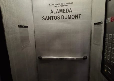 Capa para elevador cinza instalada na cabine, com placa Alameda Santos Dumont