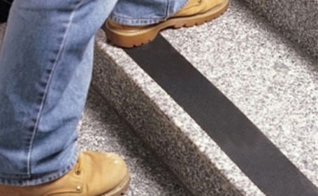 Pessoa de botas subindo escada com fita antiderrapante preta nos degraus