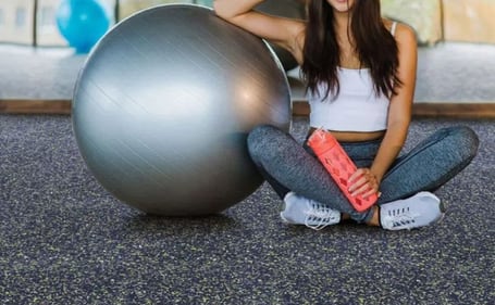 Mulher sentada em piso de borracha de academia com bola de pilatés Mulher sentada em piso de borracha de academia com bola de pilatés