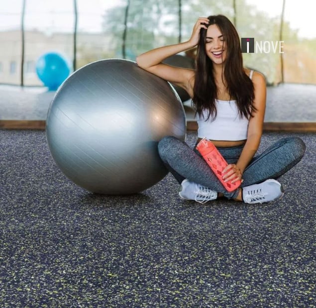 Mulher sentada em piso de borracha de academia com bola de pilatés