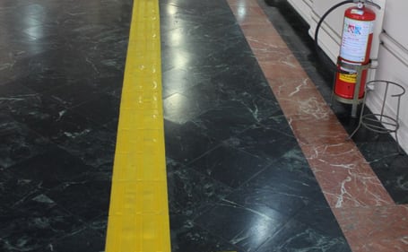 Piso tátil direcional amarelo sobre piso de mármore em um corredor