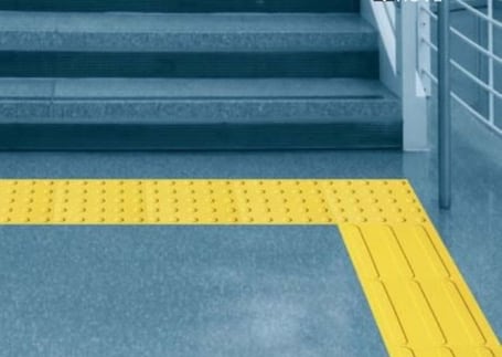 Piso tátil de alerta amarelo sinalizando o acesso a uma escada