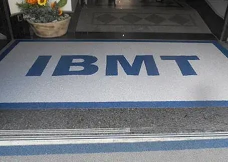 Tapete emborrachado cinza com sigla azul em entrada corporativa
