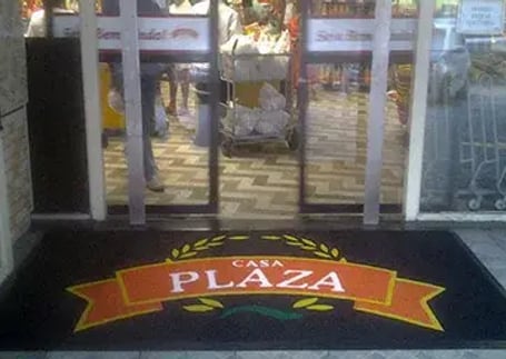 Tapete emborrachado preto com logo laranja na entrada de loja com portas de vidro